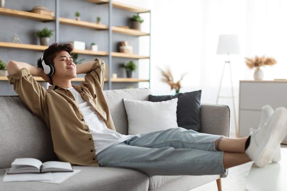 Positiv A imagem tem um homem de meia-idade sentado no sofá, sorrindo e acenando para a câmera de um notebook.